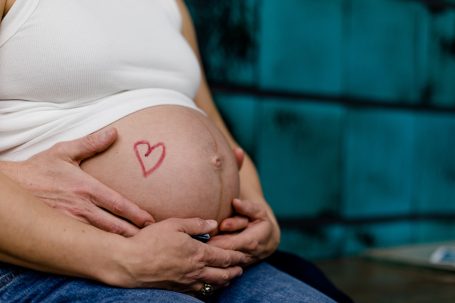 Schwangere Person hält ihren Bauch mit einem Herzchen darauf.