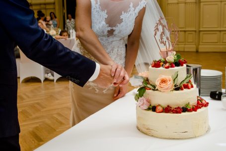 Braut schneidet eine mehrstöckige Hochzeitstorte mit Blumen und Früchten.
