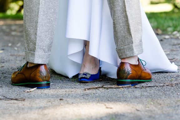 Braune Schnürschuhe und blaue Absatzschuhe unter einem Hochzeitskleid.