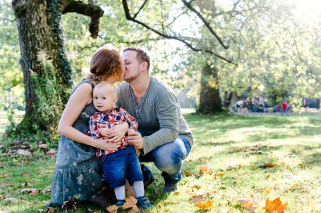 Familie im Freien: Eltern küssen sich, während sie ihr kleines Kind im Arm halten.