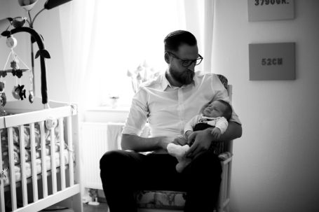 Vater hält sein Baby in einer ruhigen Ecke eines Zimmers mit einem Kinderbett.