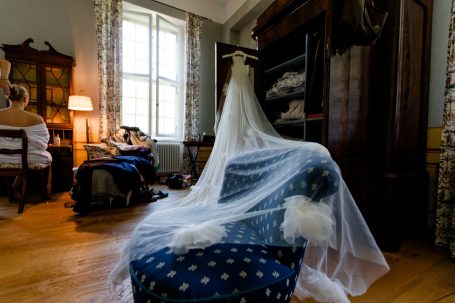 Ein Raum mit einem Hochzeitskleid auf einem Stuhl und einem antiken Schrank im Hintergrund.