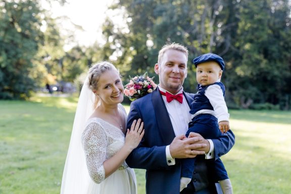 Hochzeitspaar posiert mit einem Kleinkind in einem Park im Freien.