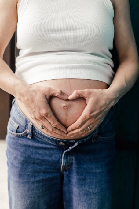 Schwangere Person formt mit Händen ein Herz über dem Bauch.