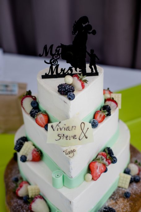 Dreistufige Hochzeitstorte mit frischen Beeren und einer dekorativen Figur obenauf.