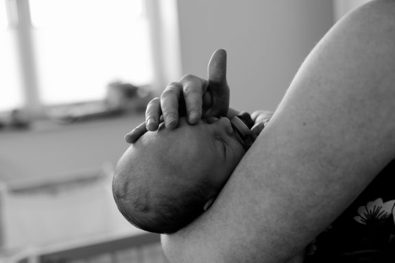 Händchen eines Erwachsenen hält den Kopf eines schlafenden Babys.