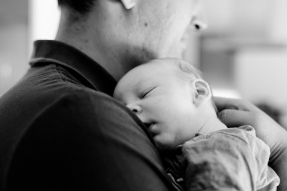 Ein schlafendes Baby liegt entspannt im Arm eines Erwachsenen.