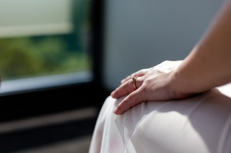 Hand mit einem Ring, die auf einem Kleid sitzt, vor einem unscharfen Hintergrund.