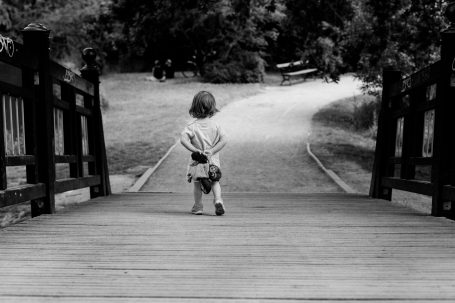 Ein Kind steht auf einer Holzbrücke und schaut einen Weg entlang.