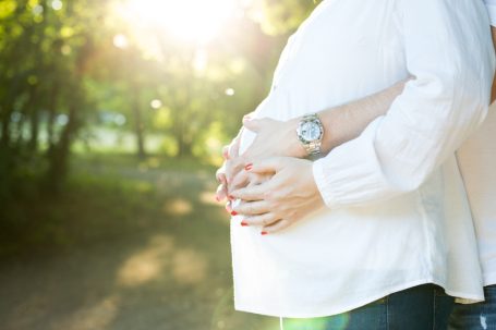 Schwangere Frau umarmt ihren Bauch, umgeben von sanftem Sonnenlicht.