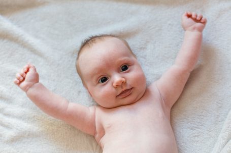 Ein säuglingsartiges Baby liegt auf einer weichen Decke und hebt die Arme.