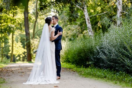 Junges Brautpaar umarmt sich romantisch in einer grünen Parklandschaft.