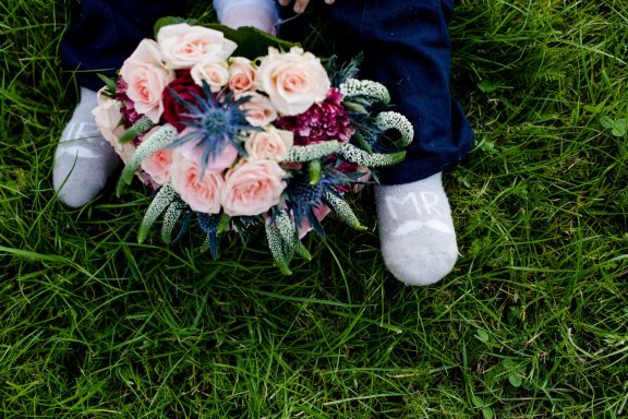 Person mit einem Blumenstrauß aus rosa Rosen und grünen Pflanzen, auf Gras stehend.