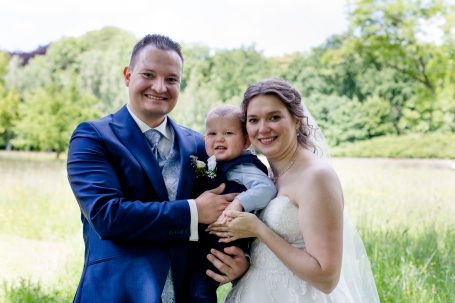 Glückliche Familie im Freien: Braut, Bräutigam und Baby in sonniger Landschaft.