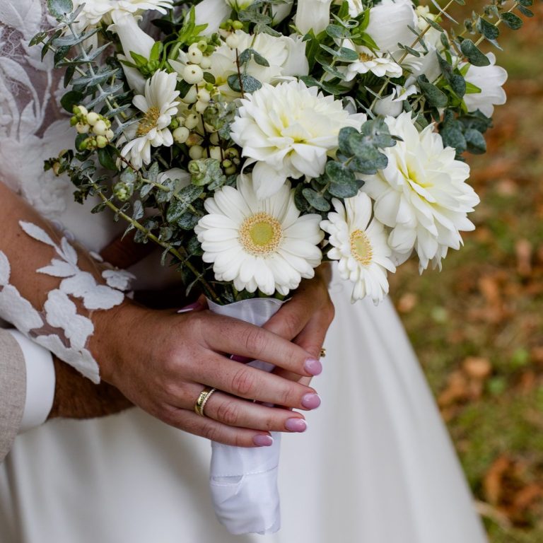 Braut hält einen Blumenstrauß mit weißen Blumen und Grünpflanzen in der Hand.